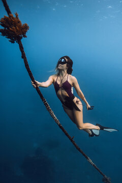 Woman freedive underwater holding rope in calm blue water
