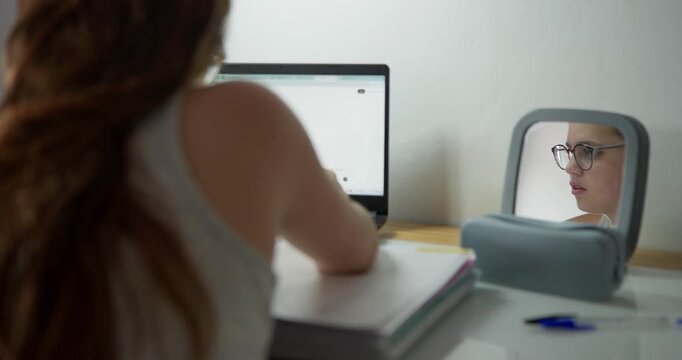 Reflection of Diligence: A young woman with long red hair focused on her laptop, with a portable mirror reflecting her thoughtful expression, highlighting the introspective side of learning and work.
