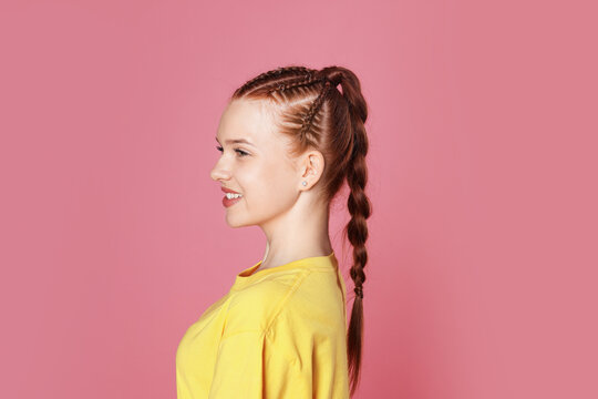 Smiling teenage girl with beautiful braids on pink background