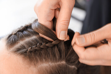 Naklejka premium Hairstylist braiding teenage girl's hair in salon, closeup