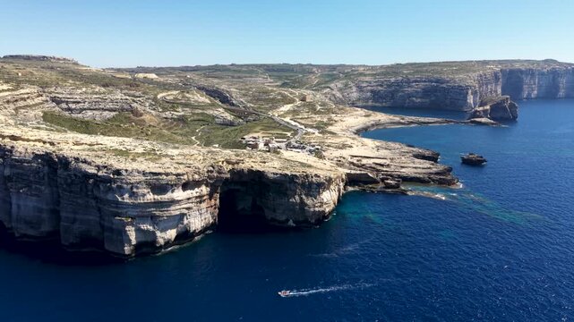 Aerial view of Dwejra Bay featuring rugged limestone cliffs, deep blue Mediterranean waters, and rocky coastal terrain in Gozo region, Malta.