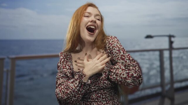 Redhead woman laughing with hands raised on ship deck, open mouth and patterned dress; joy celebration.