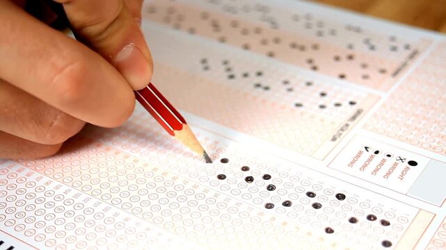 Close Up of Hand Holding Red Pencil Filling OMR Bubble Sheet for Exam