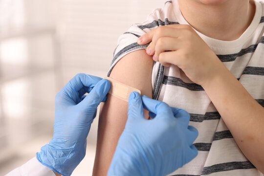 Nurse in medical gloves applying adhesive bandage onto patient's arm after vaccination indoors, closeup