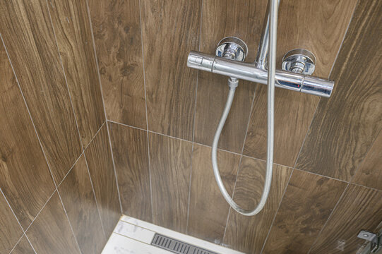 shower zone with wood-effect tiled walls, chrome thermostatic mixer, flexible hose, and a linear drain on a white marble-patterned floor