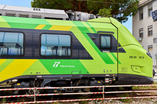 Modern Trenitalia regional train ETR 104 in bright green and yellow livery, side view of the locomotive cabin and passenger carriage on tracks.