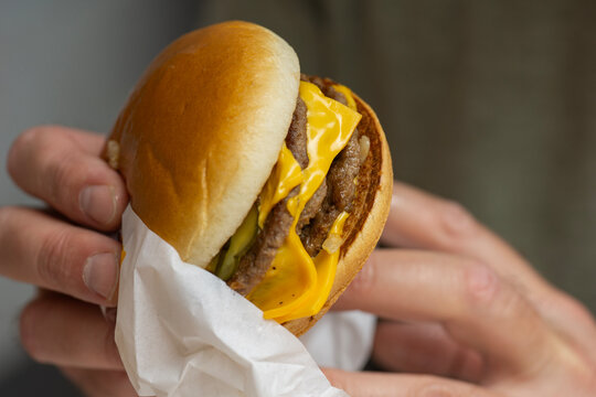 holding double cheeseburger background paper wrapper surface of hands gripping juicy beef burger with melted cheddar cheese pickles soft bun junk food fast food meal concept of gastronomy, fast food