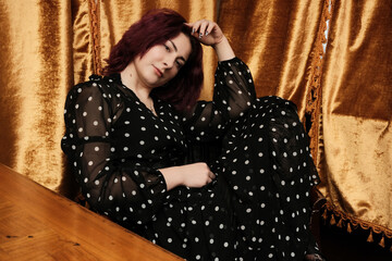 Fototapeta premium Polka dot beauty relaxes in rich golden drapery at cozy venue