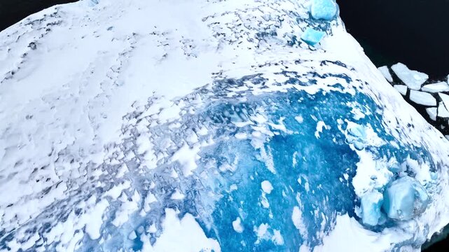 Aerial view of the textured surface of a massive iceberg with deep blue glacial ice and white snow in Tasiilaq, Sermersooq Municipality, Greenland.