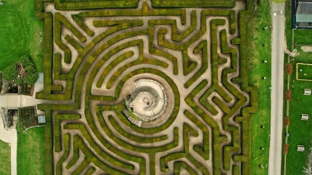 Aerial top down view of a person reaching the center of a complex green hedge labyrinth