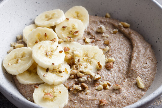 Healthy flaxseed porridge topped with banana slices, chopped nuts and seeds in a ceramic bowl. Nutritious breakfast with natural ingredients, close up view