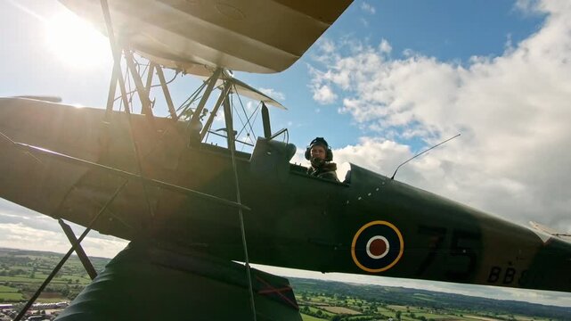 World war two military biplane flying in a cloudy blue sky with the sun flaring