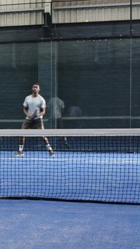 Vertical video: Incoming ball making player in grey with racket shift and swing to return at court