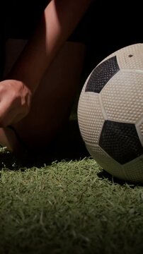 Vertical video: Hands rising player kneeling in cleats tying laces on turf steadying ball to play