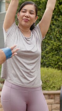 Vertical video: Warming up woman taking grey band and pulling overhead on patio in grey top