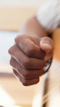 Vertical video: Focus as man plucking acoustic guitar strings, thumb strumming, practicing at home