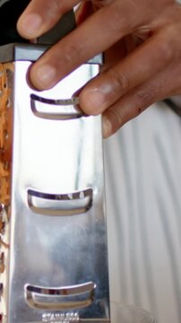 Vertical video: Grating man holding grater, pressing carrot making shreds in kitchen with bracelet