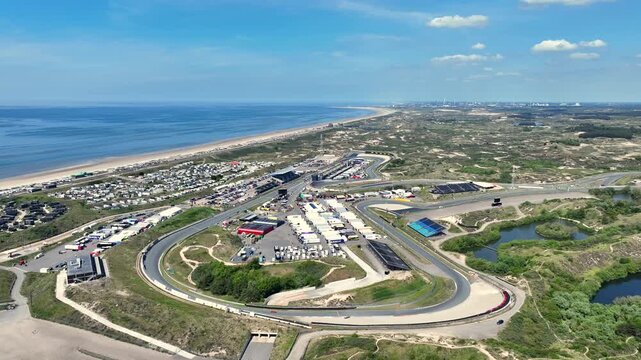 Aerial view of MASCOT Circuit Zandvoort race track nestled among coastal dunes and the North Sea beach under a clear blue sky in Zandvoort, Noord-Holland, Netherlands.