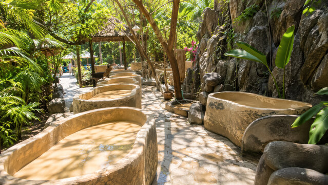 Stone mud bath tubs arranged in shaded tropical spa garden .generative AI