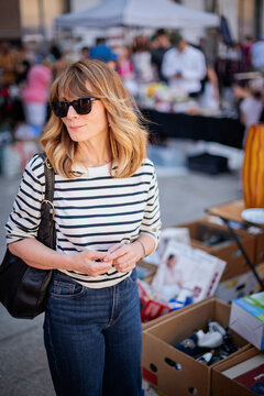 Stylish midlife woman browsing items at outdoor flea market on a sunny day