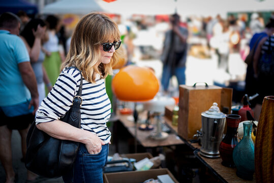 Stylish midlife woman browsing items at outdoor flea market on a sunny day