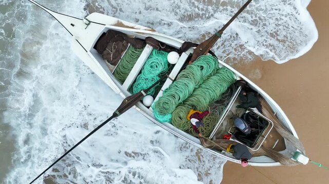 Aerial view of a traditional fishing boat with fishermen inside filled with green nets and oars on the sandy shore of Praia de Mira, Coimbra, Portugal.