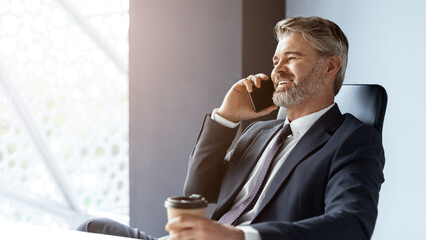 Smiling Middle Aged Caucasian Man In Suit Engaged In Phone Conversation While Sitting At Modern...