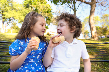 Fototapeta premium Cute little kids eating ice cream together on chairs in park