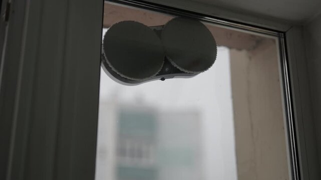 Robotic window washer automatically cleaning dirty glass surface inside apartment. Concept of modern smart home technology for domestic chores and simplifying household maintenance.