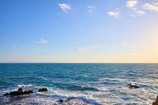 Serene ocean horizon at sunset with rocky shoreline and clear blue sky