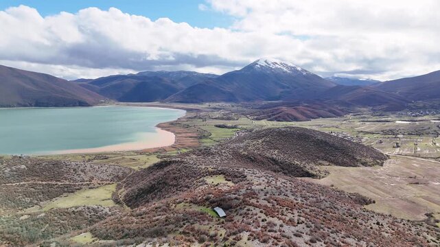 Aerial drone camera moving forward high over Lake Prespa, North Macedonia, revealing green agricultural plains, rural wetlands, and a dramatic snow-covered mountain peak