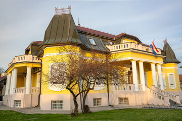 Obraz premium Employment Agency Vinkovci, Yellow Villa With Classical Columns And Red Roof Facing Symmetrical Garden And Walkway