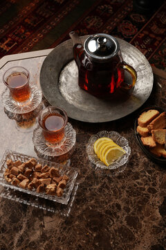 Traditional armudu glasses with black tea, teapot, lemon slices, jam, nuts, dried fruits, and sugar cubes on a table. Authentic eastern hospitality and tea culture concept
