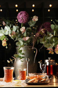 Traditional armudu glasses with black tea, teapot, lemon slices, jam, nuts, dried fruits, and sugar cubes on a table. Authentic eastern hospitality and tea culture concept