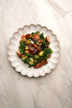 High angle view of gourmet roasted quail pieces served with potatoes, mushrooms, fresh greens, and rich brown gravy in a ceramic plate on a marble table. Elegant restaurant poultry dish