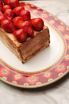 Close-up of a gourmet baked Alaska or meringue dessert topped with fresh juicy strawberries, served on an elegant red patterned platter over a marble table. Luxury restaurant sweet pastry