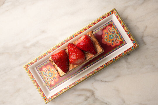 Close-up of a gourmet baked Alaska or meringue dessert topped with fresh juicy strawberries, served on an elegant red patterned platter over a marble table. Luxury restaurant sweet pastry