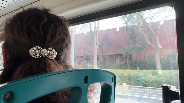 female passenger gazing out the window of a public bus as it travels through a quiet winter town in China. A small hair ornament decorates her hair while empty streets and subdued urban scenery