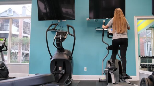 Fit woman working out on elliptical trainer machine in the gym