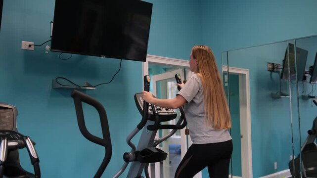 Young woman exercising on elliptical machine in gym