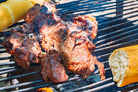 Costillas de carne vacuna cocin&aacute;ndose lentamente sobre parrilla durante proceso de asado argentino