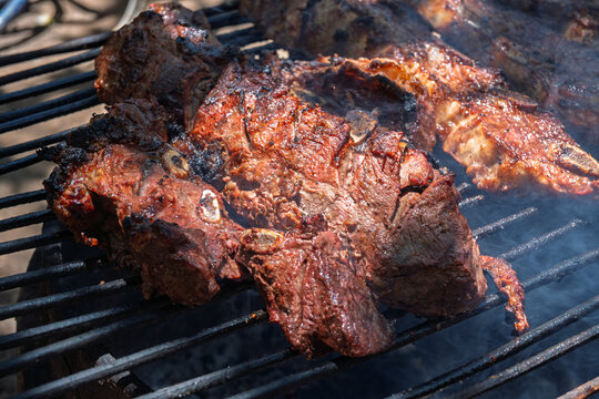 Costillas de carne vacuna cocin&aacute;ndose lentamente sobre parrilla durante proceso de asado argentino