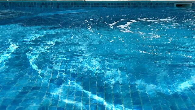 Clear blue swimming pool with shimmering light reflections on tiled surface.