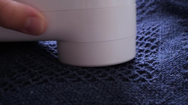 Close-up of a fabric shaver removing lint from a dark knit blanket