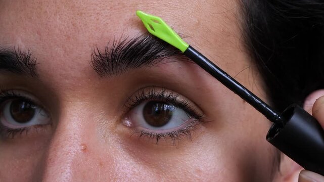 Close-up of a woman grooming her eyebrow with a green brush applicator