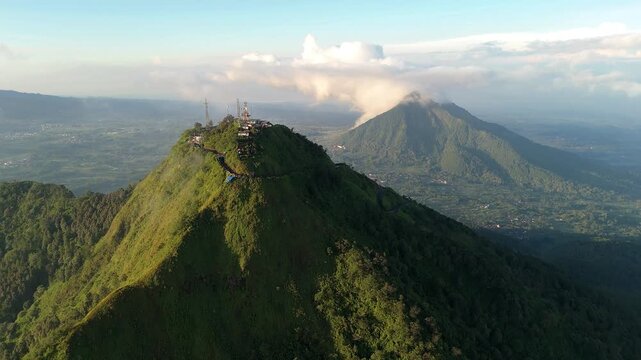 Aerial view of Mount Telomoyo with communication towers on the summit and volcanic peaks under a cloudy sky in Magelang, Central Java, Indonesia.