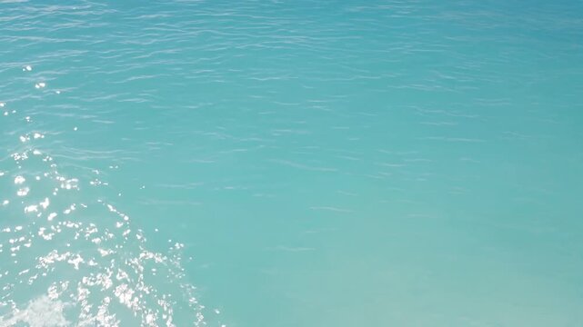 Crystal clear turquoise ocean water surface with gentle ripples and shimmering sun reflections creating a serene and tranquil background for a summer vacation scene