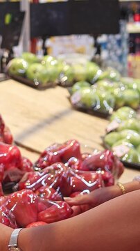 Woman choosing packaged water apples in supermarket produce section. Selecting fresh tropical fruits from retail display, slow motion shopping scene, consumer purchase decision.