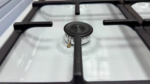 White gas stove cooktop closeup showing burner and black iron grate, glossy enamel surface with tiny droplets, low angle bottom