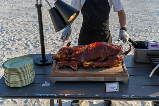 Chef Carving Whole Roasted Suckling Pig on Cutting Board at Beach